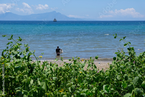 A local fisherman throwing a net fishing in the blue ocean with tropical island of Atauro Island in the distance, Timor Leste, South East Asia photo