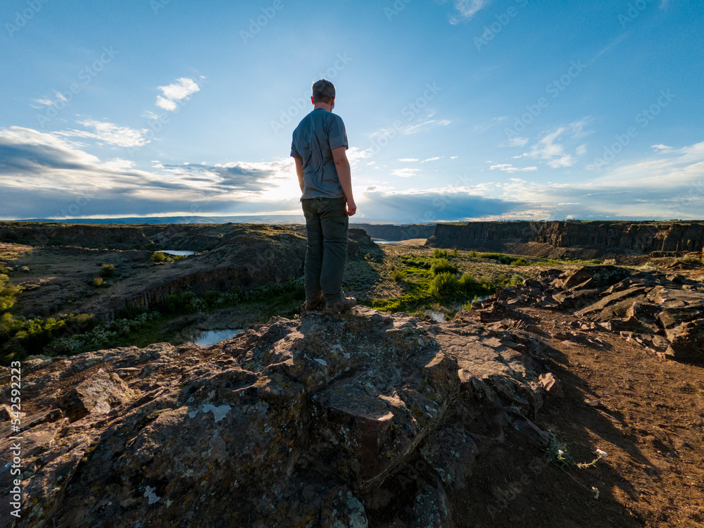 Fototapeta premium Athletic adventurous male hiker standing on a ridge looking down into a valley along the Columbia River.