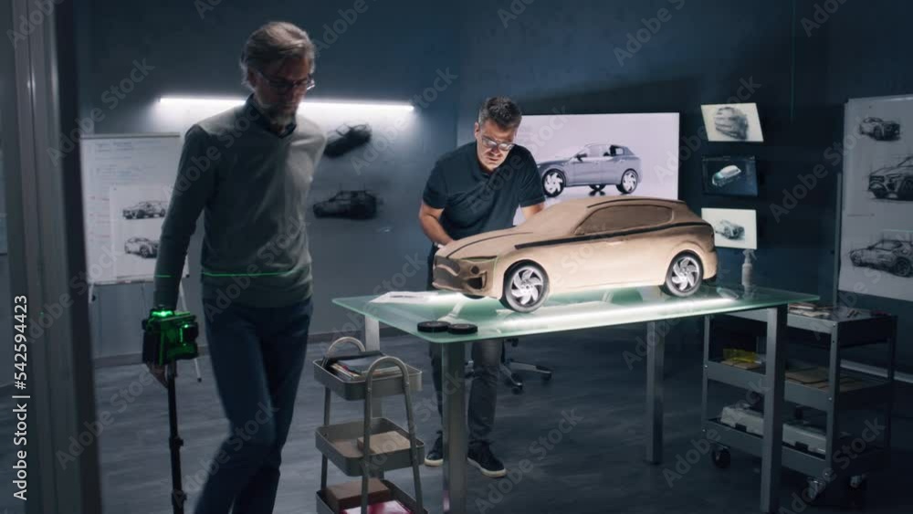 Two male automotive designers working on eco friendly model of electric car in modern car design studio. One sculpting with plasticine clay, other working in 3D modeling computer software. Two male automotive designers working on eco friendly model of electric car in modern car design studio. One sculpting with plasticine clay, other working in 3D modeling computer software.