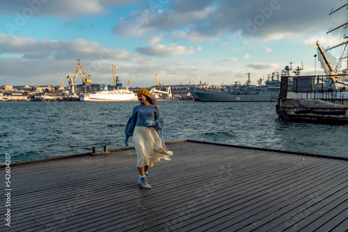 Outdoors fashion portrait of a beautiful middle aged woman walking on the beach. Marine background. Dressed in a stylish warm blue sweater, yellow skirt and beret. © svetograph