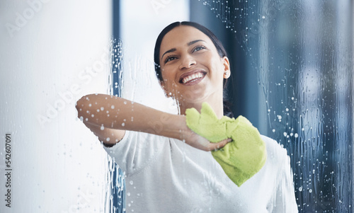 Cleaning, glass and hygiene with a black woman using a cloth or rag while wiping a window in an office. Cleaner, janitor or housekeeper washing a transparent surface with soap and water photo