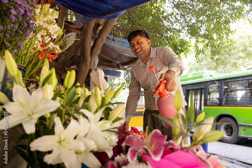 Male florist spraying water on flower in shop  photo