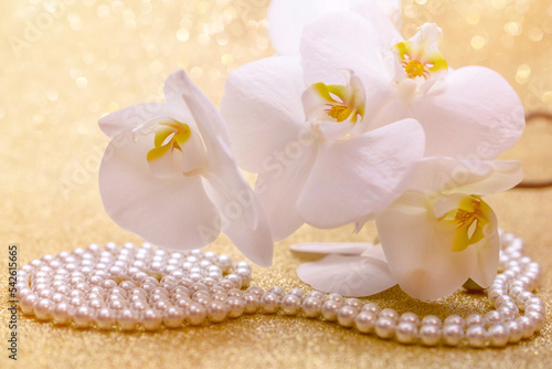 white Orchid and pearl necklace on a shiny gold background 