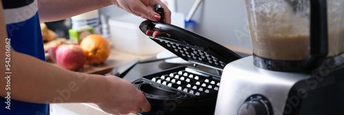 Woman opens electric waffle maker for Viennese and Belgian waffles. photo