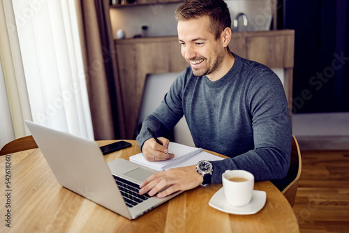 A happy man following online course on a laptop from home. photo