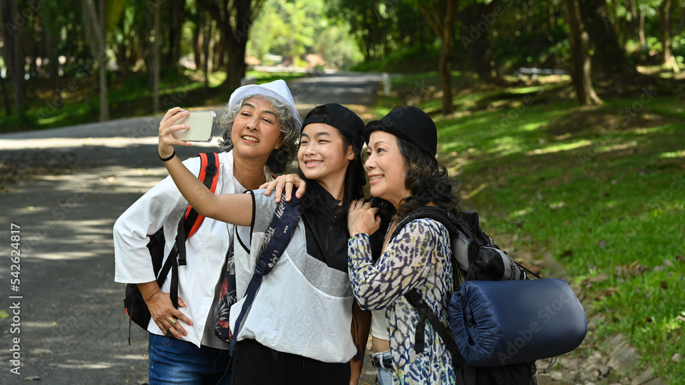 Joyful asian girl with holding smartphone and taking selfie with lovely elderly women while walking in the park Joyful asian girl with holding smartphone and taking selfie with lovely elderly women while walking in the park