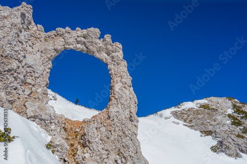 A hole in the rock with a hiker seen in the background - Hajduk Gates on Cvrsnica Mountain with snow in the winter photo