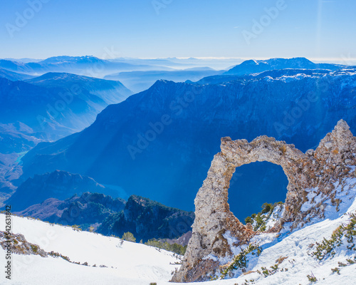 A hole in the rock with a beautiful view of the mountains and the river in the valley - Hajduk Gates on Cvrsnica Mountain with snow in the winter photo