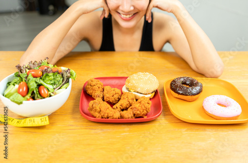 Beautiful female stop eat fried chicken junk food and make healthy food choices greens vegetable salad in weight loss diet and wellness on table. Woman chooses clean food for breakfast. Diet concept.