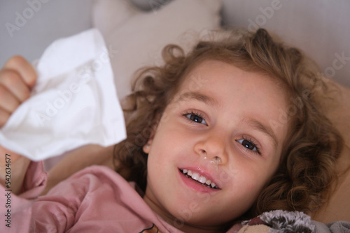 Sick girl wiping her nose with a tissue in her hand lying on the bed. seasonal virus, cold, catarrh photo