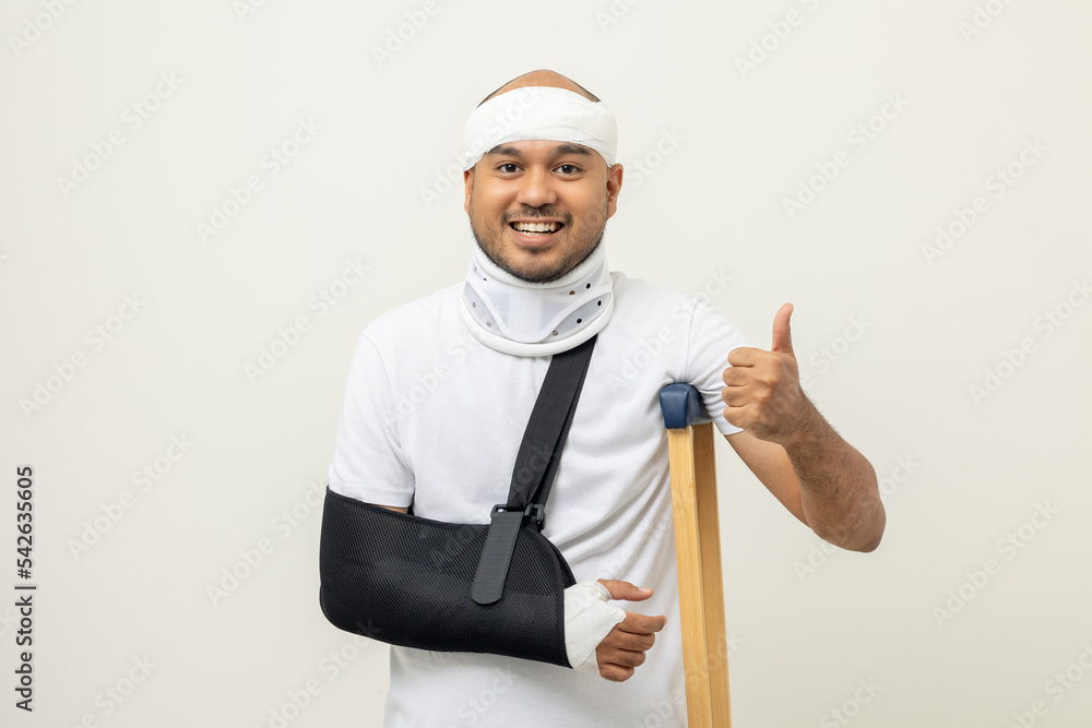 Happy young asian man broken arm and leg on isolated. Man put on plaster cast splint with walking sticks crutches. Patient wearing sling support arm with neck collar. life insurance and accident Happy young asian man broken arm and leg on isolated. Man put on plaster cast splint with walking sticks crutches. Patient wearing sling support arm with neck collar. life insurance and accident