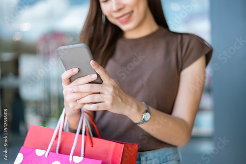 Enjoy Beautiful woman with shopping bag using cell phone at fashion mall. Trendy female holding smartphone near window a clothes store. Women enjoying shopping lifestyle fashion