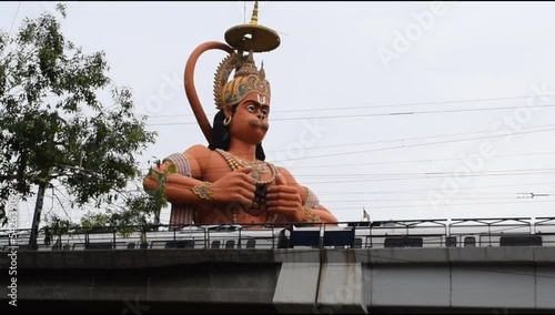Delhi metro train passing near big statue of Lord Hanuman situated near Karol Bagh, Delhi, India, Lord Hanuman big statue touching sky photo