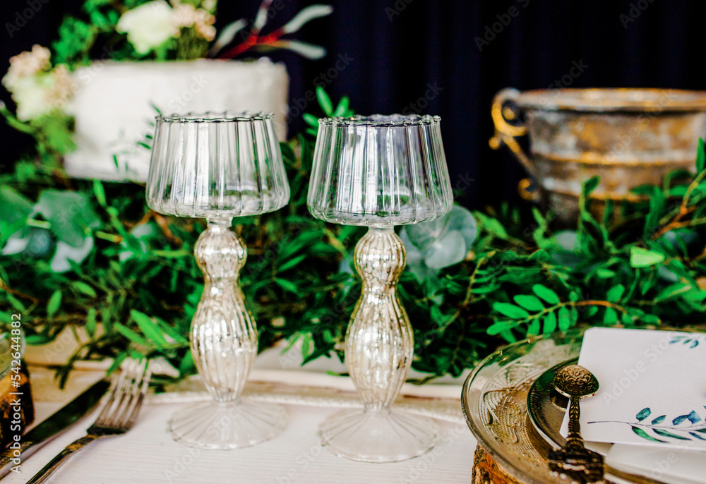 Wedding. Composition. On a wooden white table with serving dishes and glasses decorated with green flowers on a white background texture
