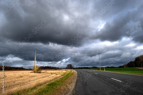 Dramatic sky with dark rain clouds over asphalt country road in autumn landscape