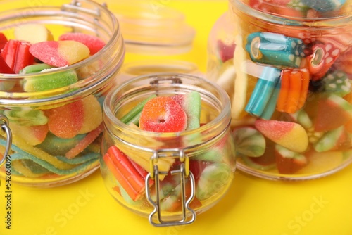 Glass jars of tasty colorful jelly candies on yellow background, closeup
