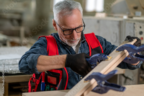 Gray-haired carpenter working in his workshop and looking involved