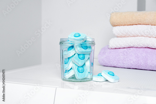 Jar with water softener tablets near stacked towels on washing machine photo