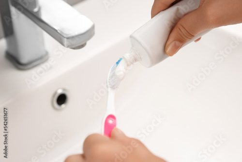 Woman applying toothpaste on brush in bathroom  closeup