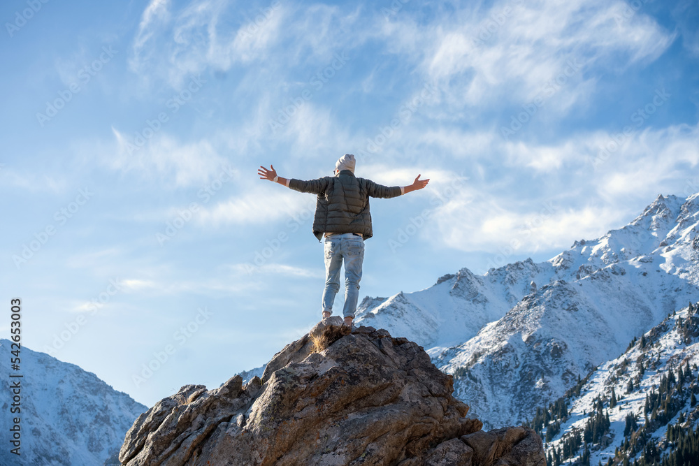 Hyped man standing on a rock surrounded by snowy mountains and sky