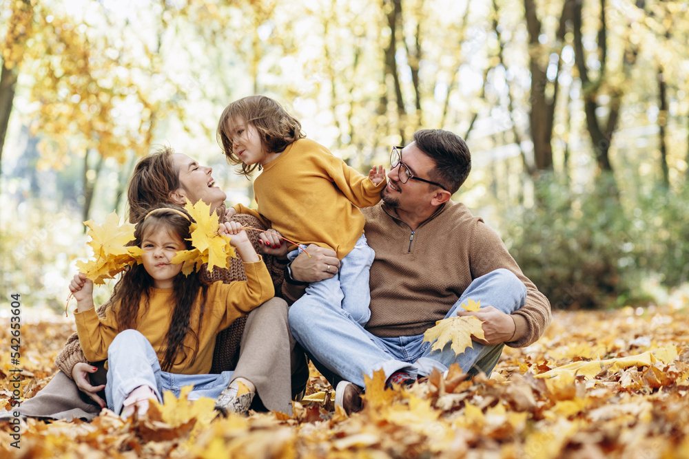 Family with two daughters sitting in park in autumn leaves Family with two daughters sitting in park in autumn leaves