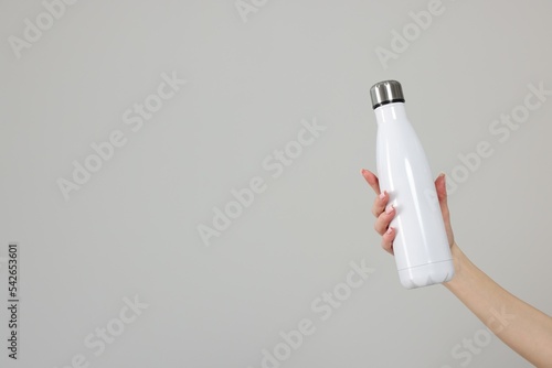 Woman holding thermos bottle on light grey background, closeup. Space for text