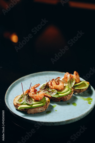 Bruschetta with avocado and shrimp, on crispy dried bread, decorated with greens.