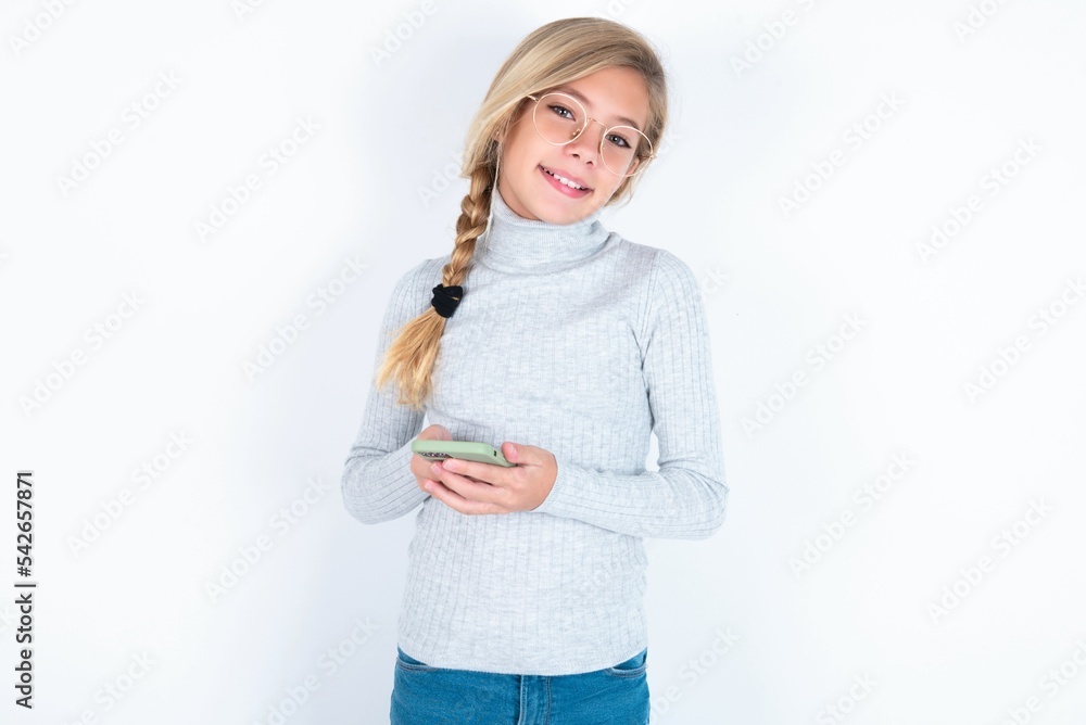 beautiful caucasian teen girl wearing gray turtleneck sweater over white wall Mock up copy space. Using mobile phone, typing sms message beautiful caucasian teen girl wearing gray turtleneck sweater over white wall Mock up copy space. Using mobile phone, typing sms message