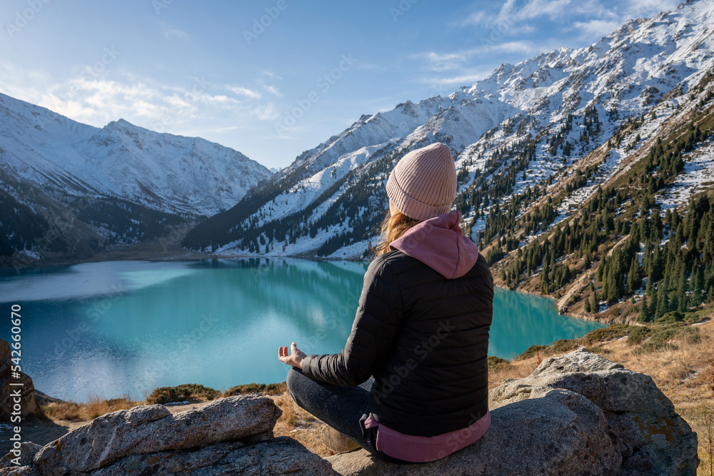 Fototapeta premium Back view of a woman meditating on a vantage point over turquoise mountain lake