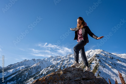 Playful woman walking on a rock, strolling surrounded by snowy mountains