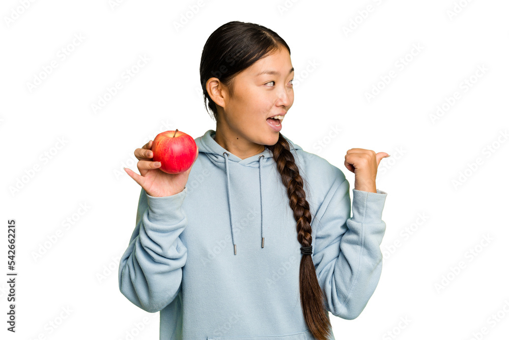 Young asian woman holding a red apple isolated points with thumb finger away, laughing and carefree. Young asian woman holding a red apple isolated points with thumb finger away, laughing and carefree.