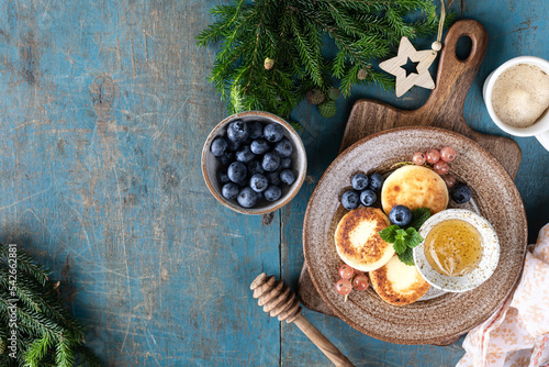 Cottage cheese pancakes, Cheesecakes with honey, currants and blueberries on a blue background. Sweet food for breakfast for the New Year