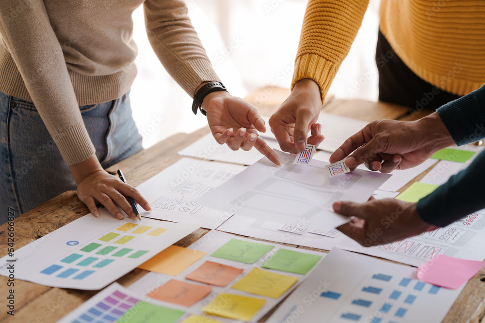 A UX design team is a confluence of user research, UX, UI design with layout paper on desk. A UX design team is a confluence of user research, UX, UI design with layout paper on desk.