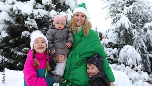 Pretty young woman in green winter coat and three little kids in winter clothes are posing together in winter garden with snow. Happiness