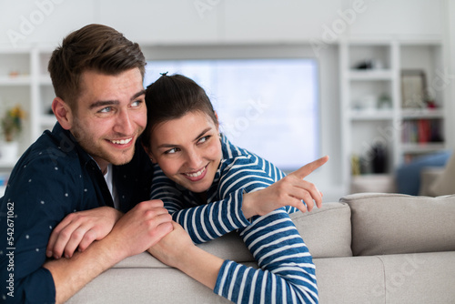 Couple Watches TV together while Sitting on a Couch in the Living Room. Girlfriend and Boyfriend embrace, cuddle, talk, smile and watch Television Streaming Services. Home with Cozy Stylish Interior. © .shock