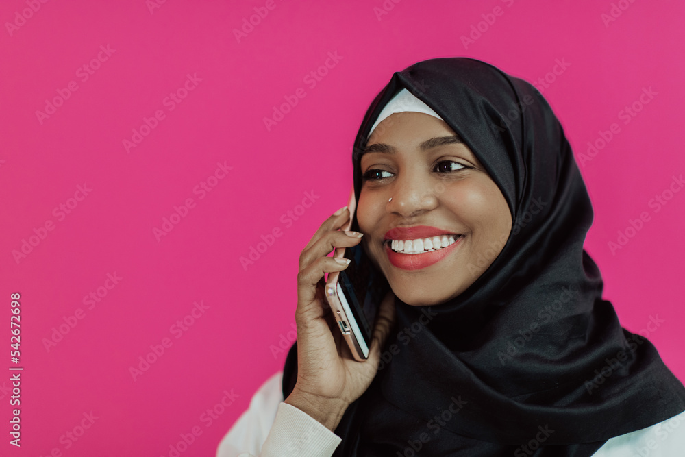 Afro woman uses a smartphone in front of a pink background Afro woman uses a smartphone in front of a pink background