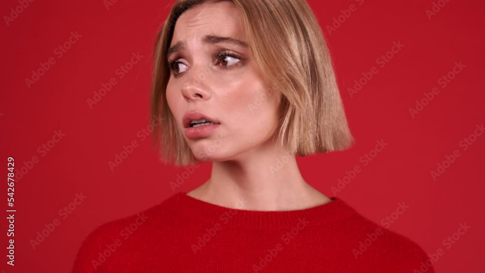 Worried blonde woman wearing red sweater looking around in the red studio Worried blonde woman wearing red sweater looking around in the red studio