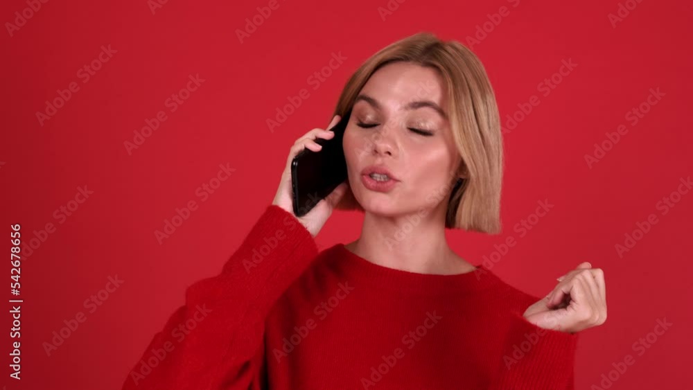 Happy blonde woman wearing red sweater talking on mobile in the red studio Happy blonde woman wearing red sweater talking on mobile in the red studio
