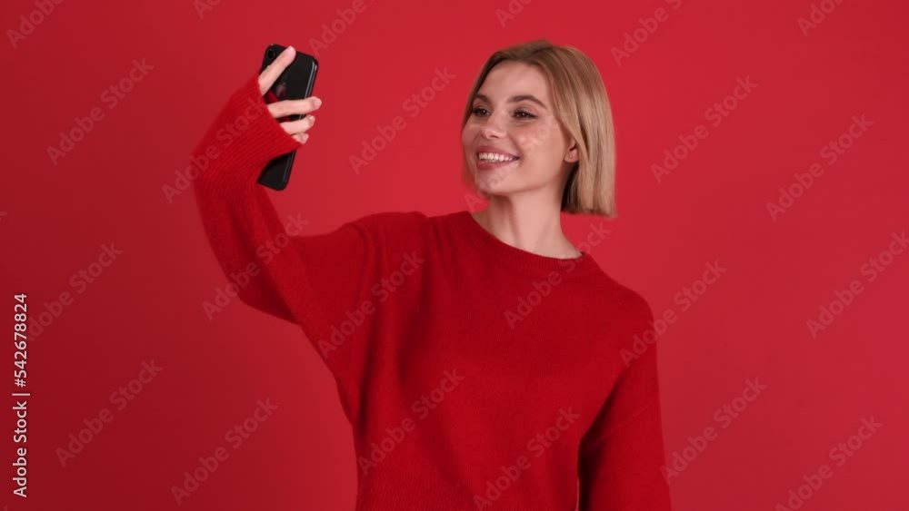 Pretty blonde woman wearing red sweater talking by video call on mobile in the red studio Pretty blonde woman wearing red sweater talking by video call on mobile in the red studio
