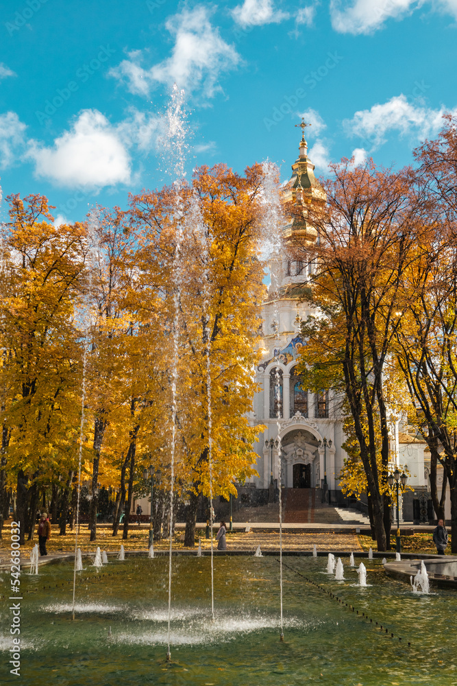 Mirror Stream fountain sight near Myrrh-bearing church with gold dome. Scenic yellow autumn sunny Kharkiv city center park with blue cloudy sky, Ukraine