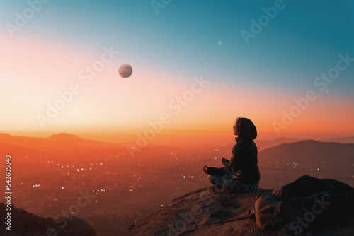 silhouette of a person sitting meditating on the top of the mountain over a valley at sunset