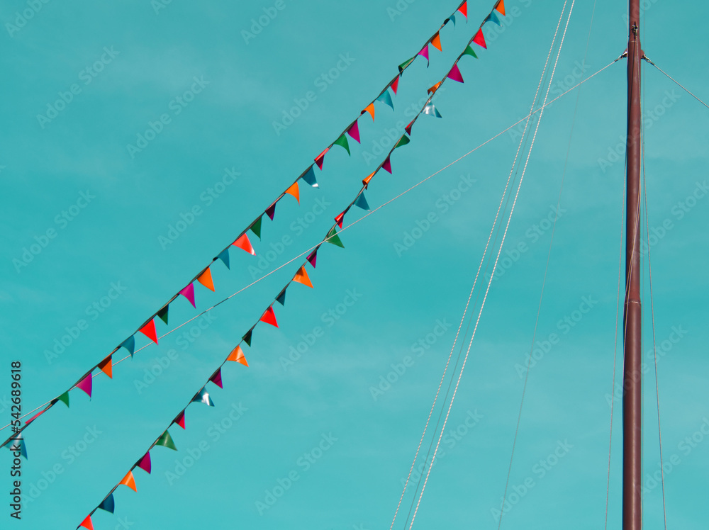 Boat mast draped in colorful flags and pennants on blue sky background
