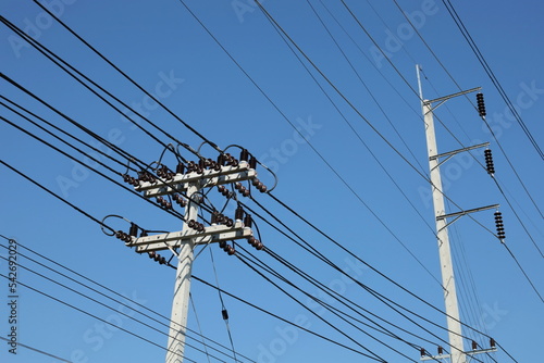 Electric poles with high voltage wires on the poles. Transmission lines with ceramic insulators suspended on metal arms of concrete poles for urban distribution on a blue sky background.