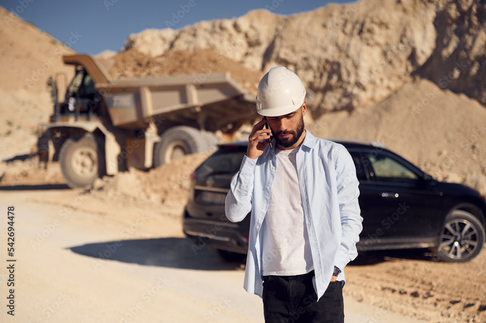 Business conversation by phone. Man in uniform is working in the quarry at daytime