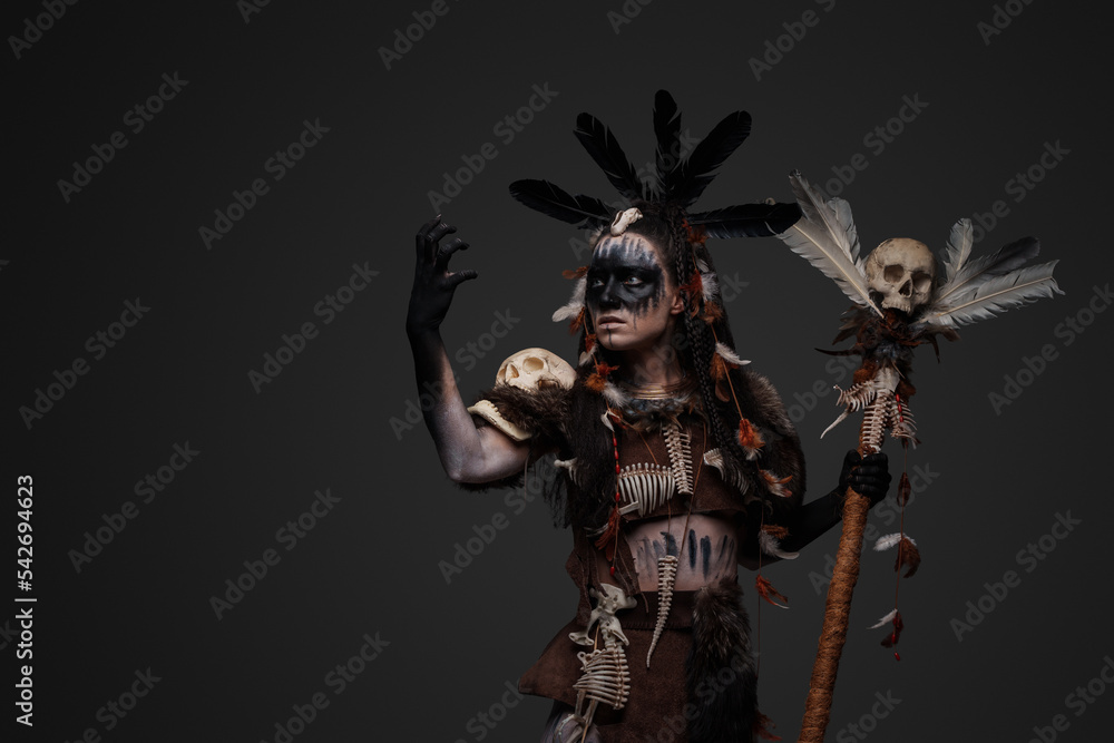 Studio shot of dark voodoo witch with painted face holding staff.