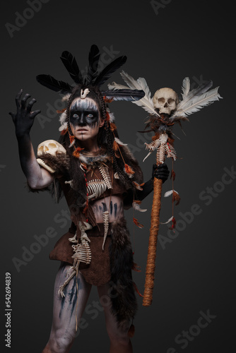 Portrait of spooky voodoo witch dressed in dark clothes holding staff with skull.