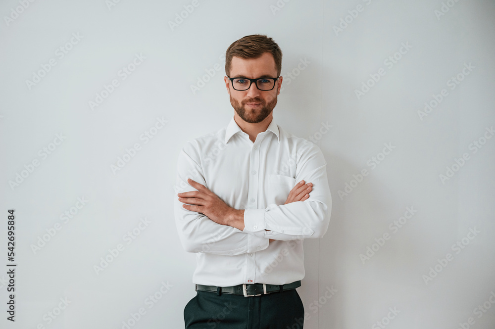 Elegant man in white shirt, black pants and in eyewear is standing against white wall Elegant man in white shirt, black pants and in eyewear is standing against white wall