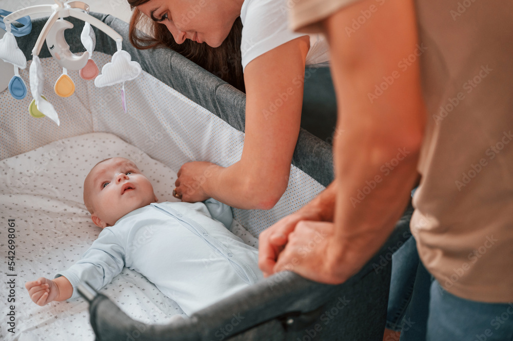 Looks down at the kids. Lovely couple taking care of newborn baby indoors at domestic room Looks down at the kids. Lovely couple taking care of newborn baby indoors at domestic room