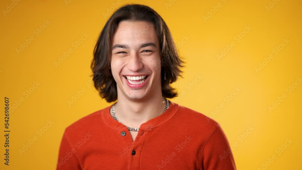 Portrait of smiling laughing, happy, handsome Hispanic gender fluid young man 20s wearing orange casual shirt isolated on yellow color background in studio. Sincere emotions lifestyle concept. Portrait of smiling laughing, happy, handsome Hispanic gender fluid young man 20s wearing orange casual shirt isolated on yellow color background in studio. Sincere emotions lifestyle concept.