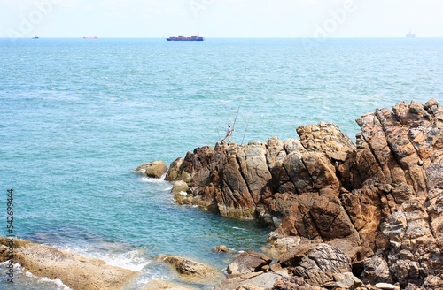 Back view of a man who stands on the top of the rock in the sea and casts his lure with his rod  for fishing at Vung Tau - Vietnam photo